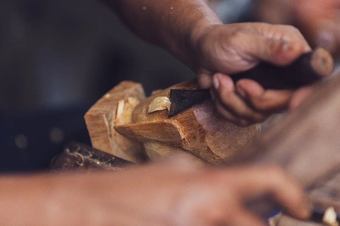 Person schnitzt Holzfigur mit Meißel